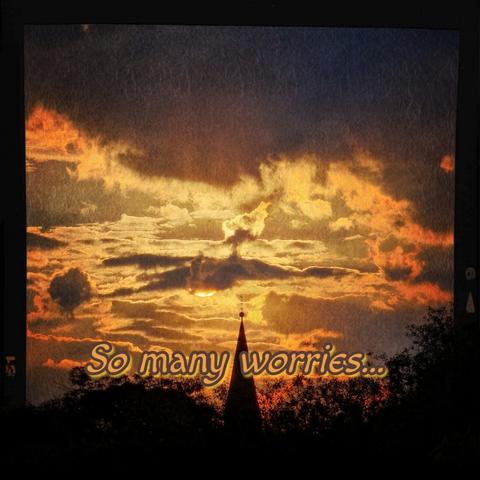A serene sunrise illuminates the sky in vibrant orange and golden hues, with clouds adding depth and texture. Silhouetted against this scene is a pointed structure, like a church steeple, standing gracefully. The foreground features the text 'So many worries...' in an elegant font, complementing the tranquil yet contemplative atmosphere.
