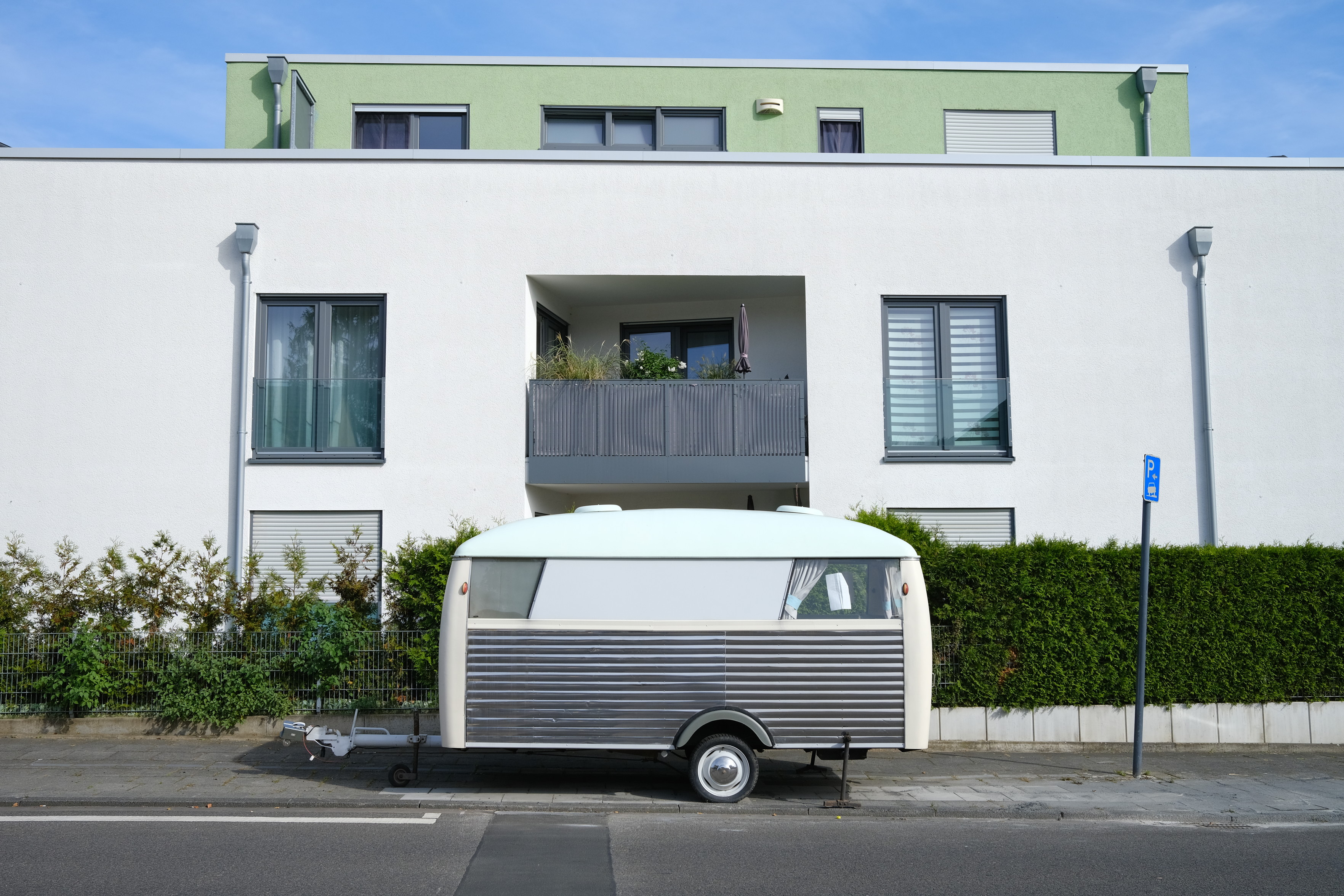 Mehrfamilienhaus in Köln Rodenkirchen, vor dem ein alter Wohnwagen steht