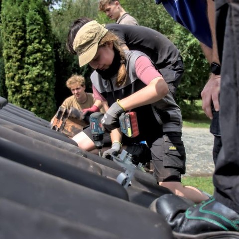 Junge Menschen auf einem Solarcamp lernen, wie Befestigungen einer Anlage an einem Schrägdach verbaut werden. 