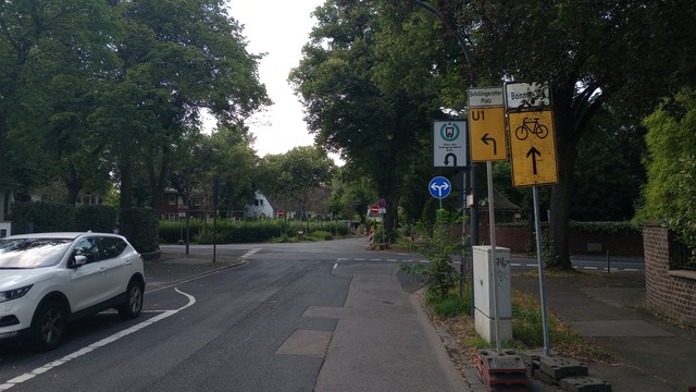 Beschilderung vor einer Baustelle: Zwei Umleitungsschilder für den Radverkehr, eins geradeaus, das andere nach links. Dahinter aber blaues Schild links/rechts und dahinter rotes Einfahrt verboten.