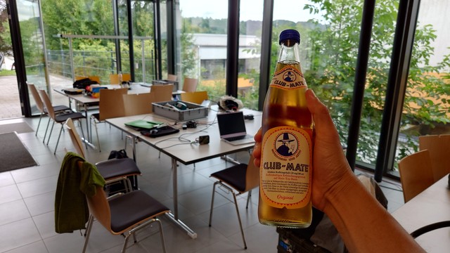 Shows hackers' drink in a venue being prepared for a hacker's evening. In the background, inside the venue, tables with technical equipment, outside the venue, green hills.
