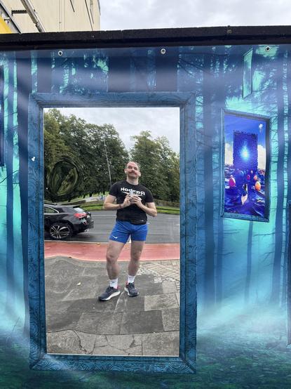 Mensch in sportlicher Kleidung macht Selfie vor riesigem, reflektierendem Spiegel in urbaner Umgebung.