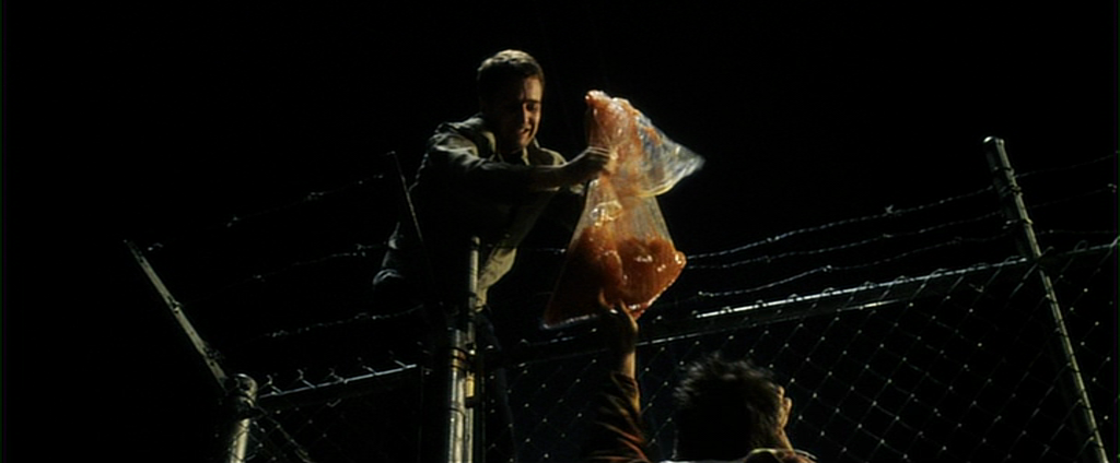 Screenshot from Fight Club (1999) in which Jack and Tyler steal bags of human fat from a liposuction clinic to make soap. One bag rips on the barbed wire fence and Tyler unsuccessfully tries to scoop up the fat with his hands.