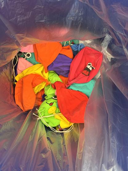 Bunte Luftballons, aus denen die Luft abgelassen wurde, mit lachenden Gesichtern, in einem großen Plastiksack.