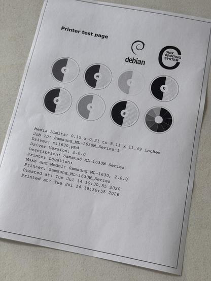 Gedruckte CUPS-Testseite mit der Überschrift ‚Printer test page’, darunter acht Farbkreise (C, M, Y, K, R, G, B und ein zwölfteiliges Graustufenrad) sowie Debian- und UNIX-Printing-System-Logos. Im unteren Bereich technische Angaben wie Media Limits, Job ID, Treiber (ml1630.ppd), Druckermodell Samsung ML-1630 und Zeitstempel.