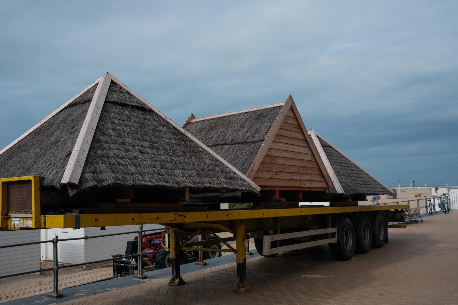 Dächer von typischen Strandhäusern liegen auf einem Anhänger, bereit zum Abtransport.